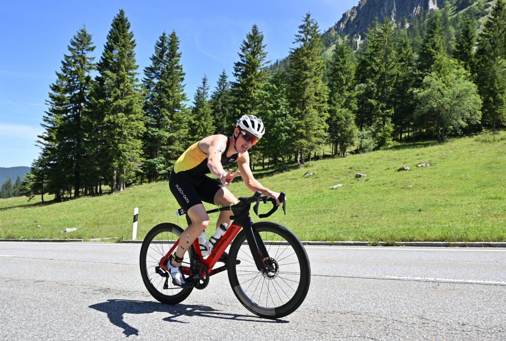 Philip Pertl fährt mit dem Rad auf dem SPitzingsattel und zeigt Peace in die Kamera. 