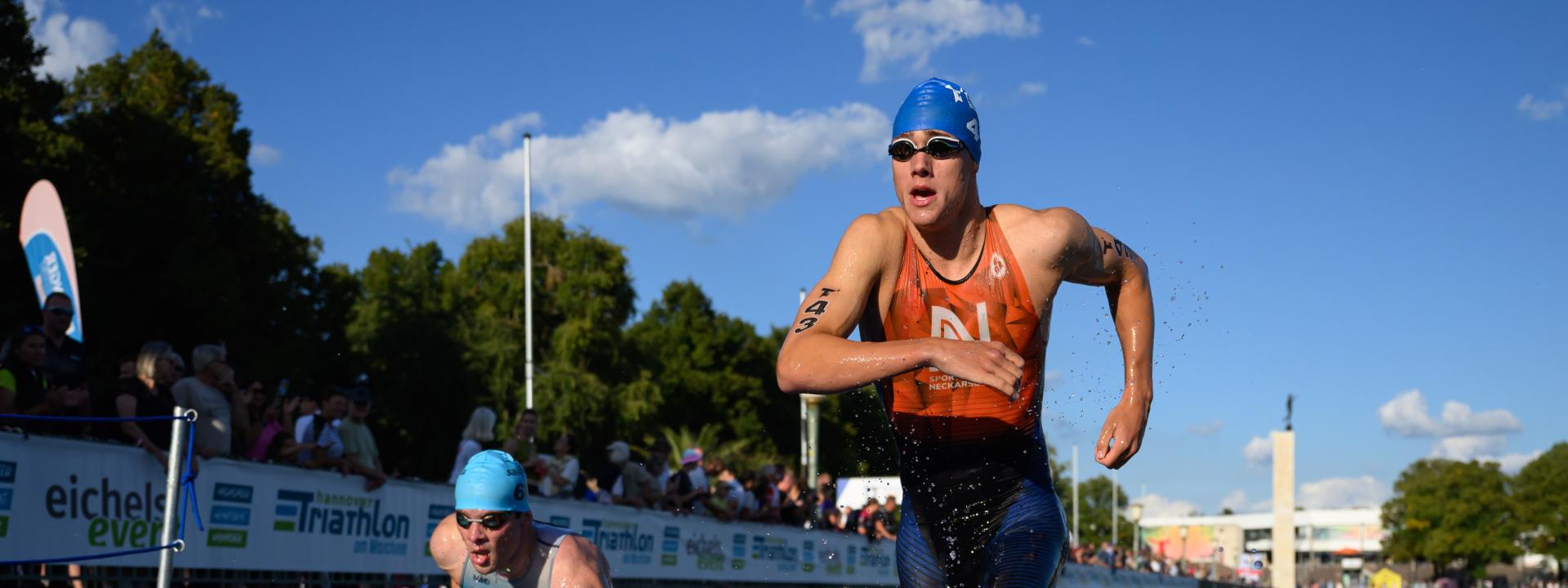 Mehrere Triathleten steigen mit Schwimmbrille über den Augen über eine Rampe aus dem Wasser