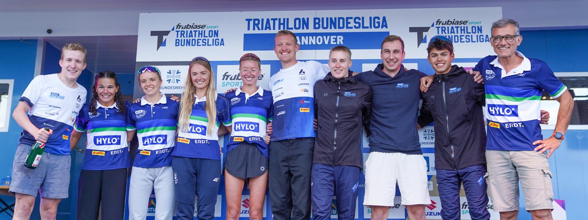 Mehrere Sportlerinnen und Sportler sowie Betreuer freuen sich nach einer Ehrung auf der Bühne über den gewonnenen Titel