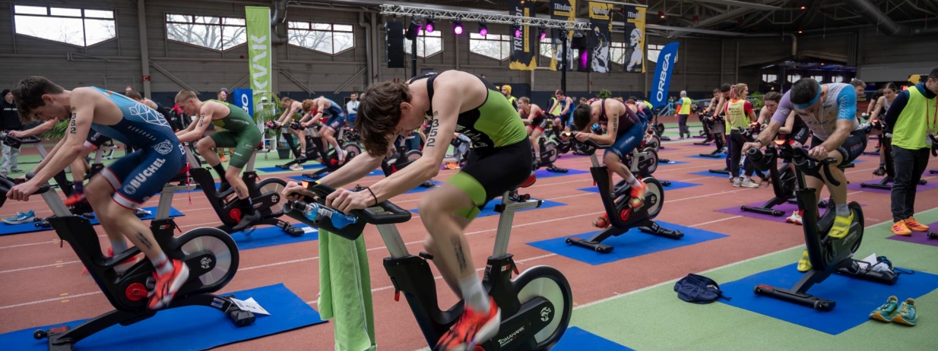 viele Sportler sitzen auf Ergometern und treten in die Pedalen