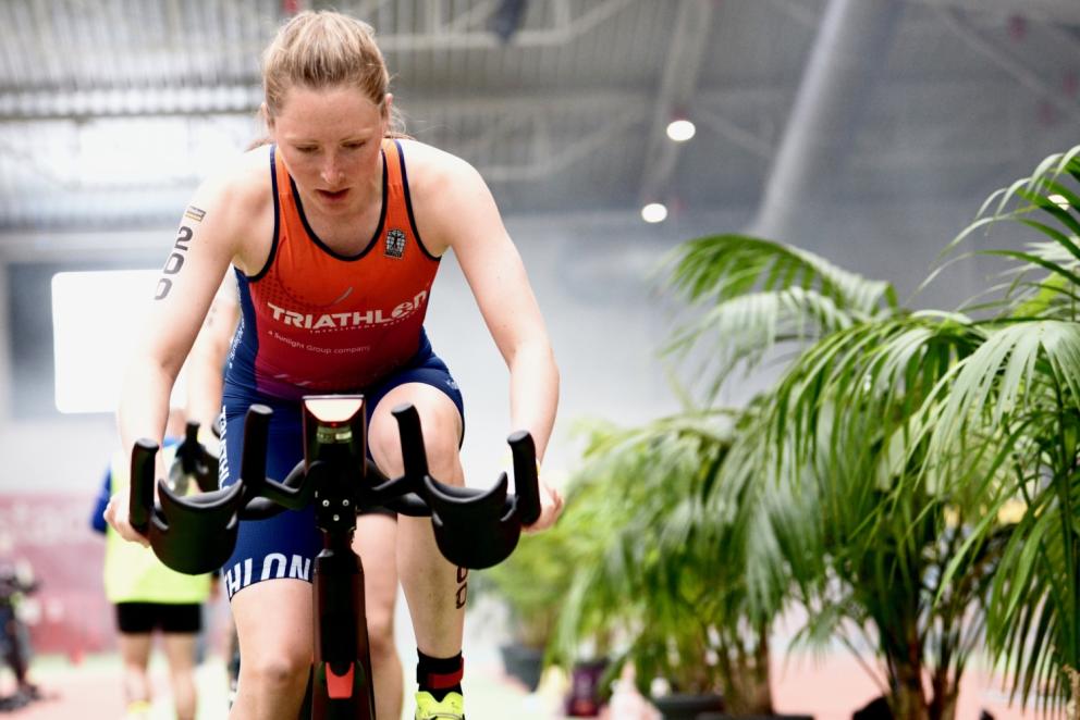 Eine sportliche Frau sitzt schwitzend auf einem Fahrrad-Heimtrainer