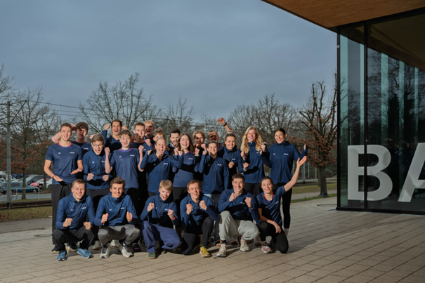 Mehrere Sportlerinnen und Sportler posieren im gleichen Auftritt für ein Teamfoto