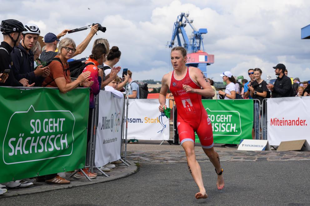 Triathletin der Dresdner Spitzen läuft um eine Kurve an Bannern vor bei mit so geht sächsisch