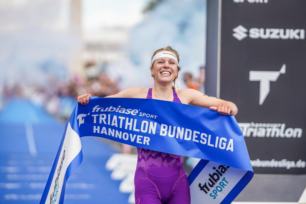 Eine Sportlerin freut sich beim Zieleinlauf mit dem Zielbanner in den Händen über ihren Sieg