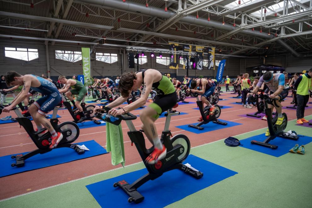 viele Sportler sitzen auf Ergometern und treten in die Pedalen