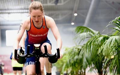 Eine sportliche Frau sitzt schwitzend auf einem Fahrrad-Heimtrainer