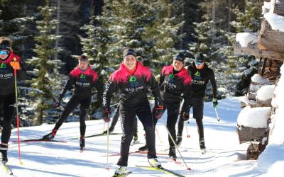 Mehrere Skilangläuferinnen und Skilangläufer fahren im seleben Team-Outfit über eine verschneite Langlauf-Loipe