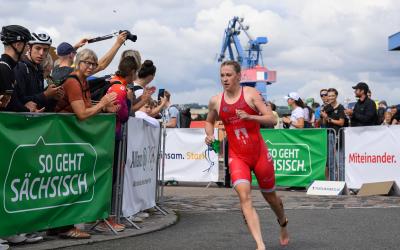 Triathletin der Dresdner Spitzen läuft um eine Kurve an Bannern vor bei mit so geht sächsisch